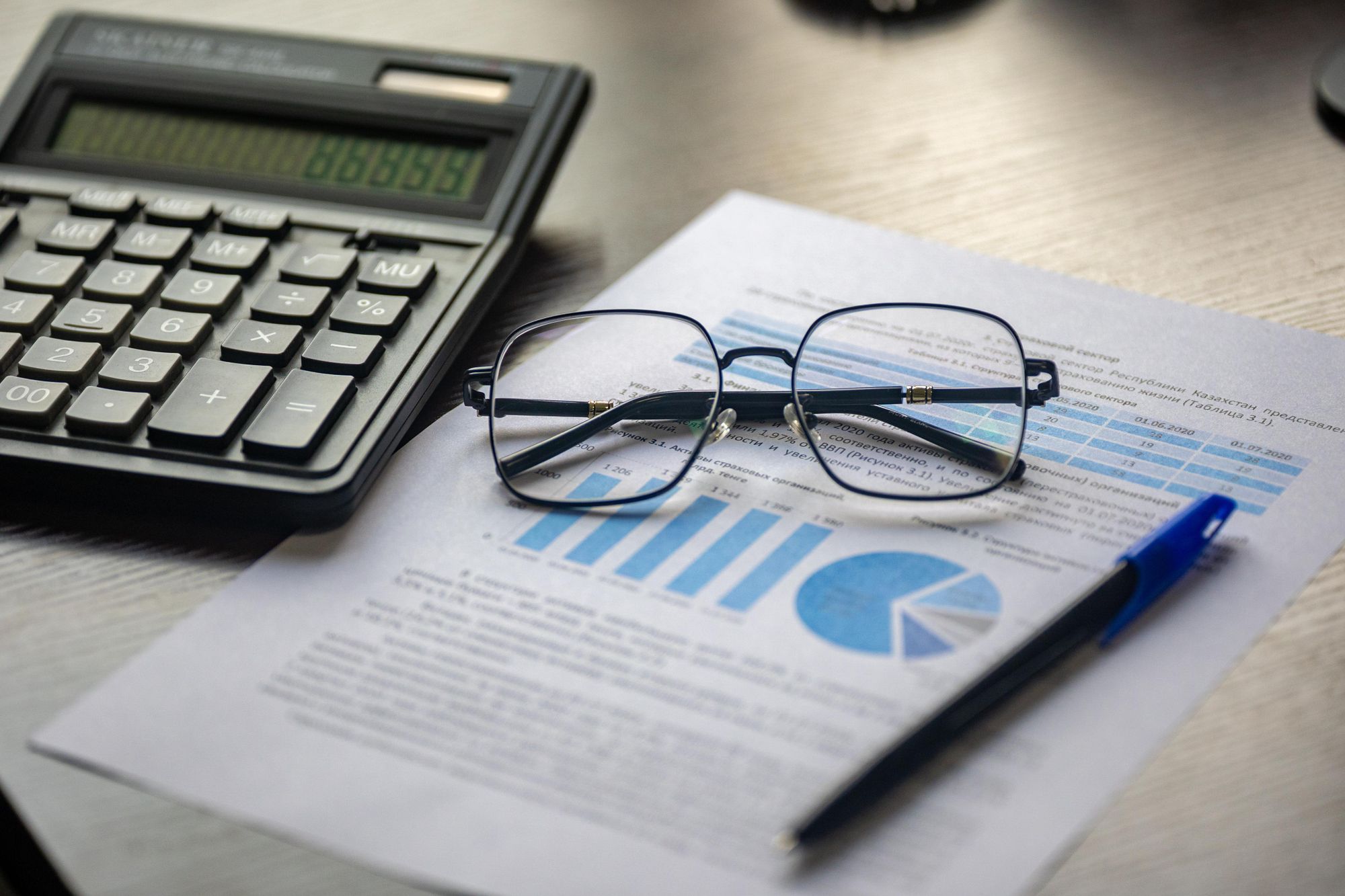 Relatório financeiro com gráficos sobre a mesa, ao lado de uma calculadora, óculos e caneta