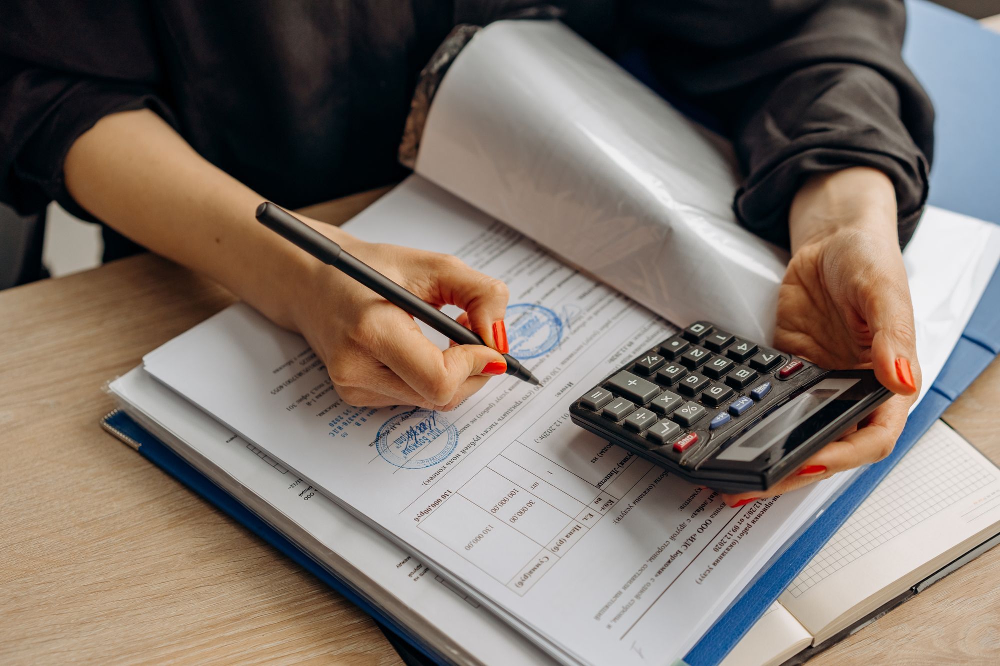Mãos de uma profissional assinando documentos ao lado de uma calculadora